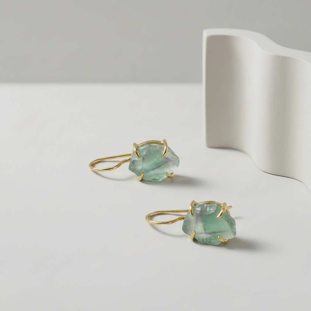Pair of raw Flourite gemstone earrings in green with gold plating hardware on a light grey background
