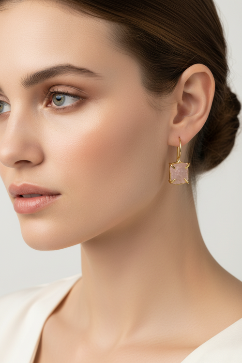 Close-up of a woman wearing a gold drop earring with raw pink gemstone on a neutral background