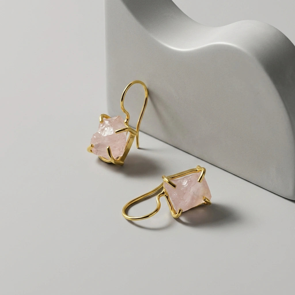 Gold plated hook earrings with raw rose Quartz gemstones on a light grey background