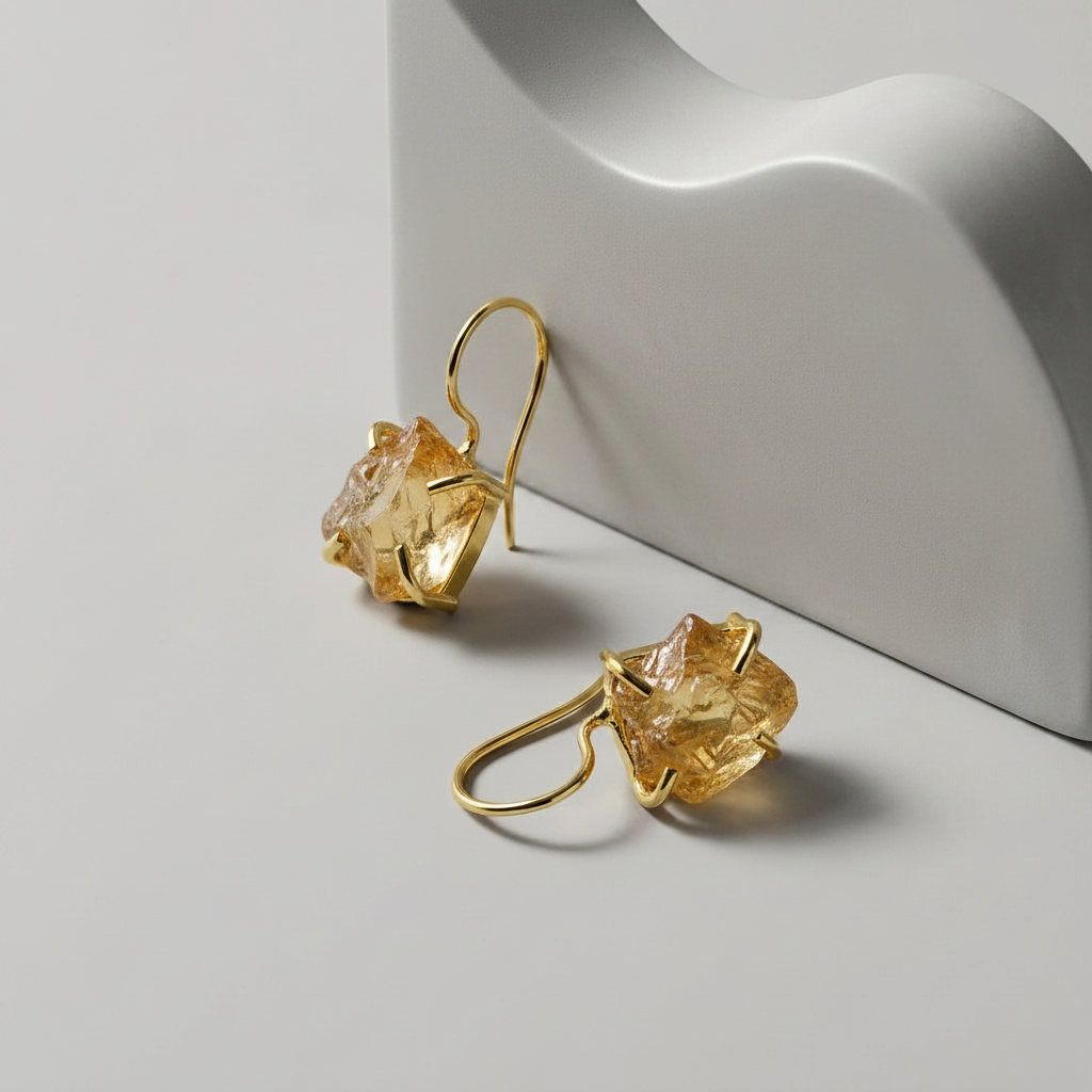 Gold hook earrings with a raw citrine gemstone on a light grey background